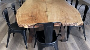 Una larga mesa de comedor con sillas, una cocina al fondo y vistas al exterior a través de amplios ventanales.