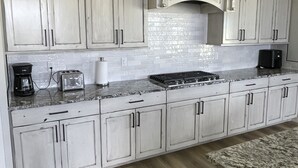 Una cocina con armarios blancos, encimera de granito, estufa y cafetera.