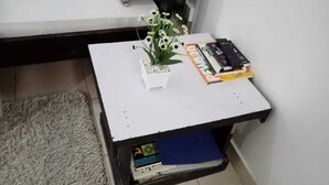 Pieni valkoinen pöytä, jonka päällä on ruukussa oleva kasvi, kaukosäädin ja kirja.