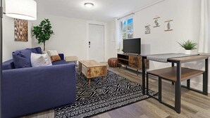 A modern living room with a blue sofa, a coffee table, a TV on a wooden stand, and a patterned rug. - Wynwood Apartments (Miami)