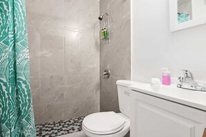 A bathroom with a toilet, a shower, and a sink with toiletries. - Wynwood Apartments (Miami)
