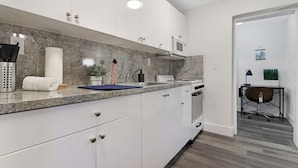 A modern kitchen with white cabinets, a granite countertop, a built-in microwave, and a stove. - Wynwood Apartments (Miami)