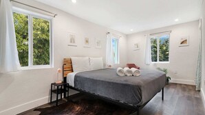 A modern bedroom with a bed, two windows, a nightstand, and a dark rug. - Wynwood Apartments (Miami)