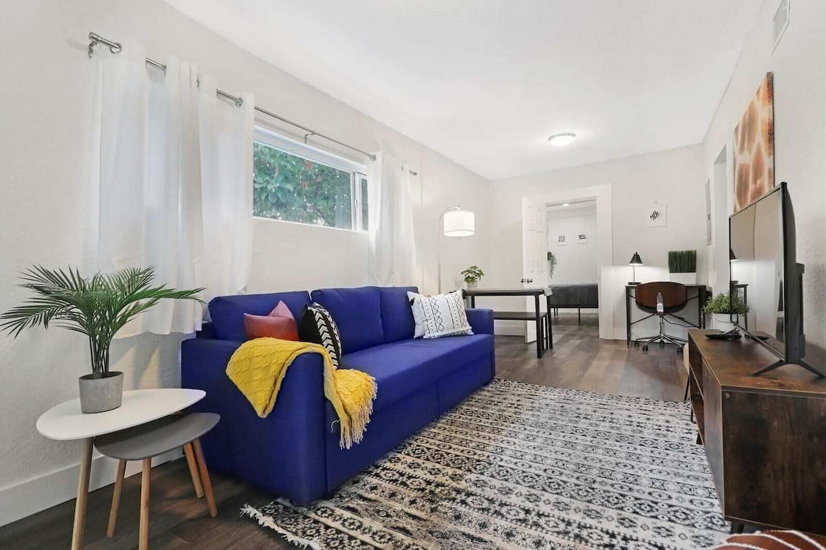A modern living room with a blue sofa, a small round table, a patterned rug, and a potted plant.