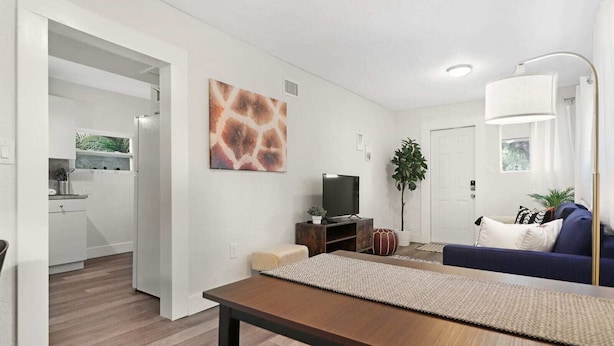 A modern living room with a sofa, a TV, and a dining area with a table. - Wynwood Apartments (Miami)