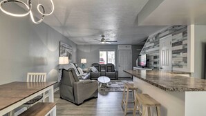 Une cuisine moderne avec un comptoir en granit, un coin repas avec une table et des bancs en bois, un canapé gris et un ventilateur de plafond.