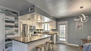 Une cuisine moderne dotée d’un grand îlot central, de meubles blancs, d’appareils électroménagers en acier inoxydable et d’un luminaire original.