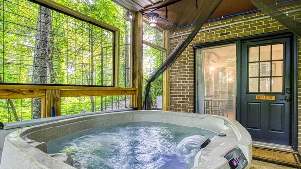 A hot tub in a covered outdoor area with a wooden deck and a brick wall. - King Suite & Private Hot Tub Great Location (Gatlinburg)