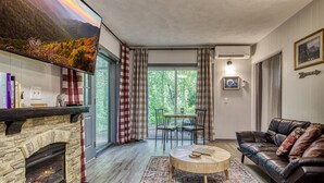 A living room with a stone fireplace, a leather sofa, a round coffee table, and a dining area with a table and chairs. - King Suite & Private Hot Tub Great Location (Gatlinburg)