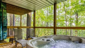 A hot tub with a waterfall feature, surrounded by wooden deck chairs and a view of a forested area. - King Suite & Private Hot Tub Great Location (Gatlinburg)