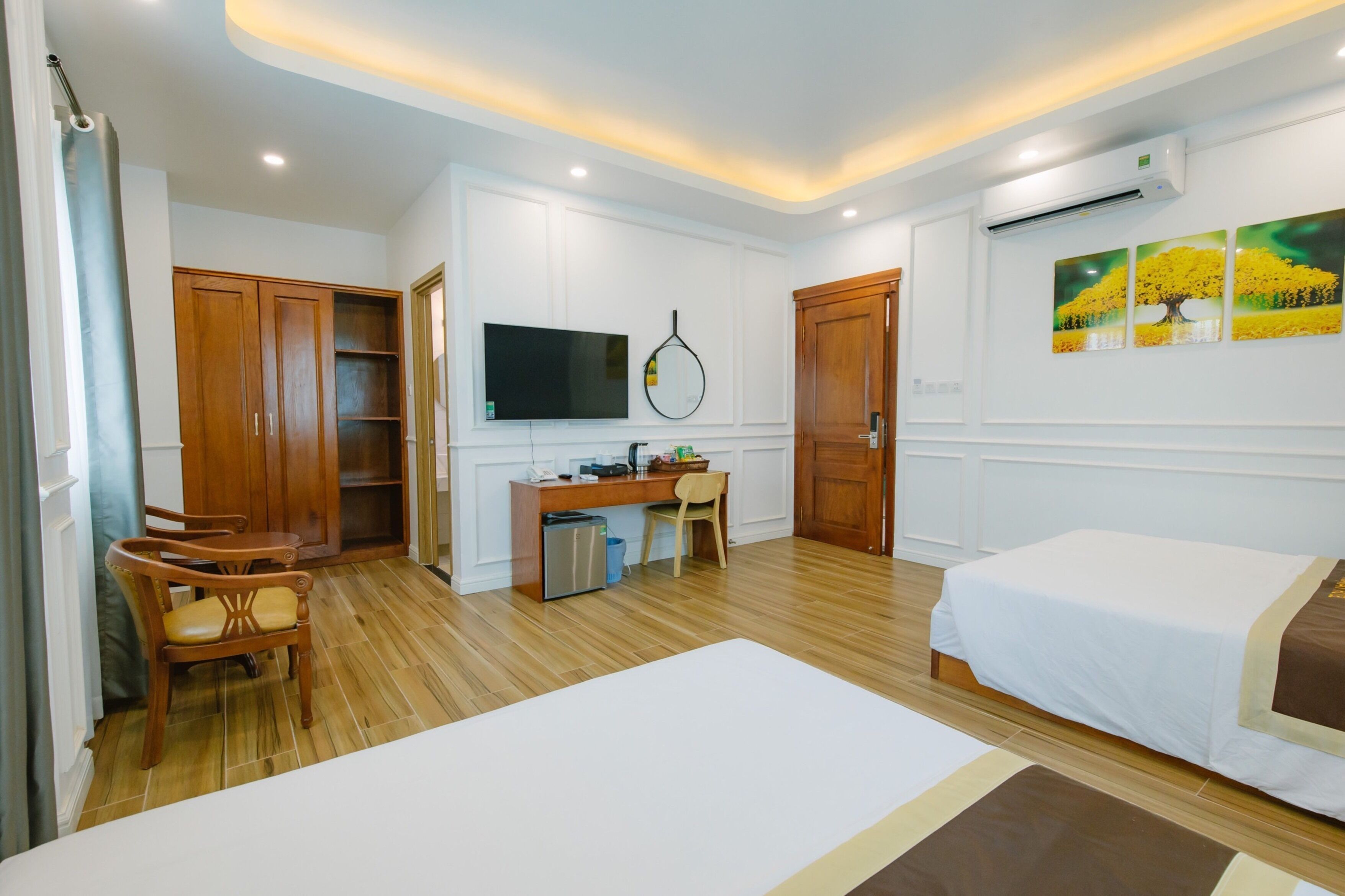 Une chambre d’hôtel équipée d’un lit, d’un bureau, d’une chaise, d’une armoire, d’une télévision et d’œuvres d’art accrochées au mur.