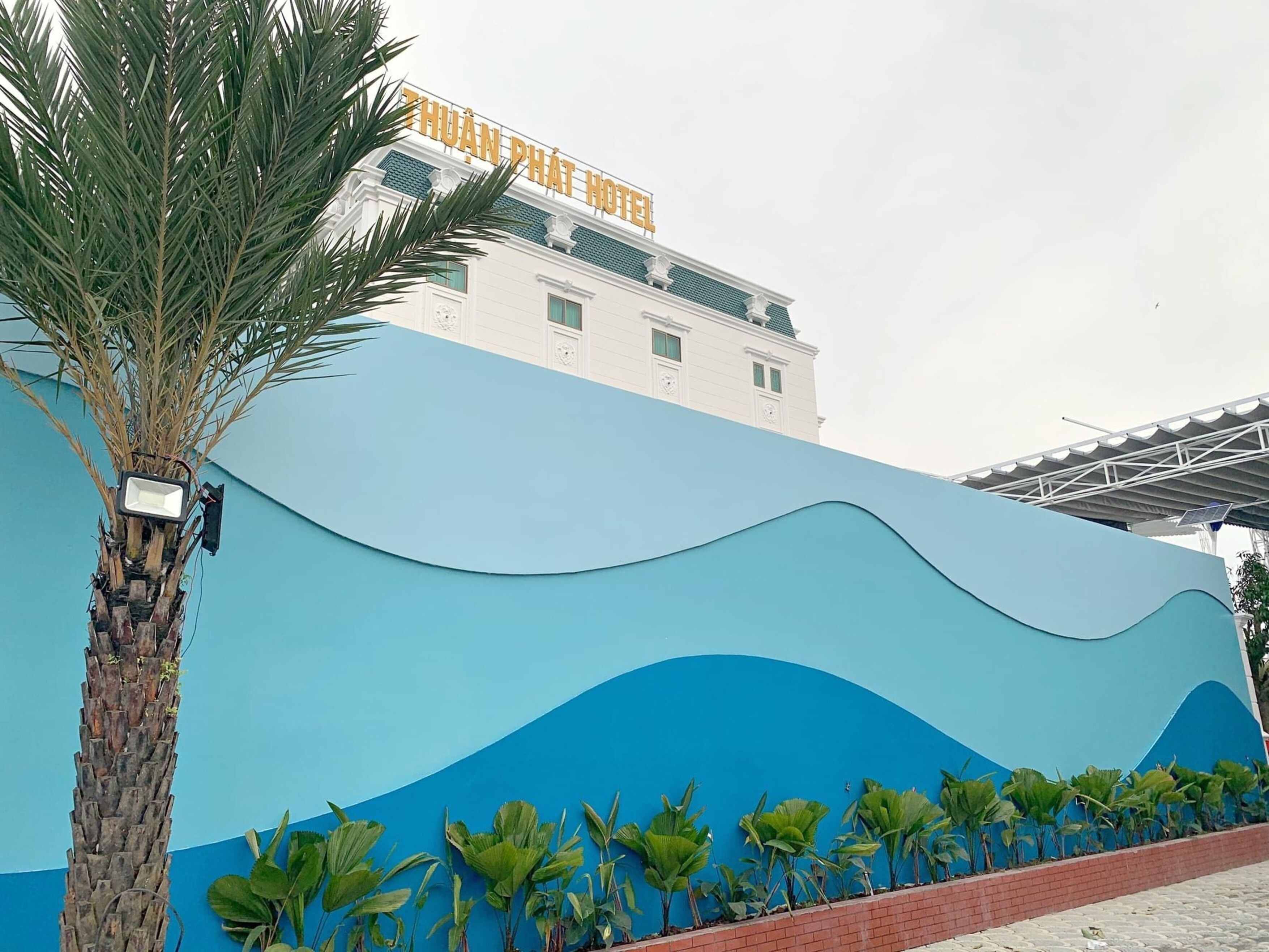 Un hotel con un diseño azul distintivo en forma de ola en su fachada, una palmera en primer plano y un cielo despejado.