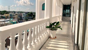 Een balkon met witte leuningen, een plant in pot en uitzicht op de stad.