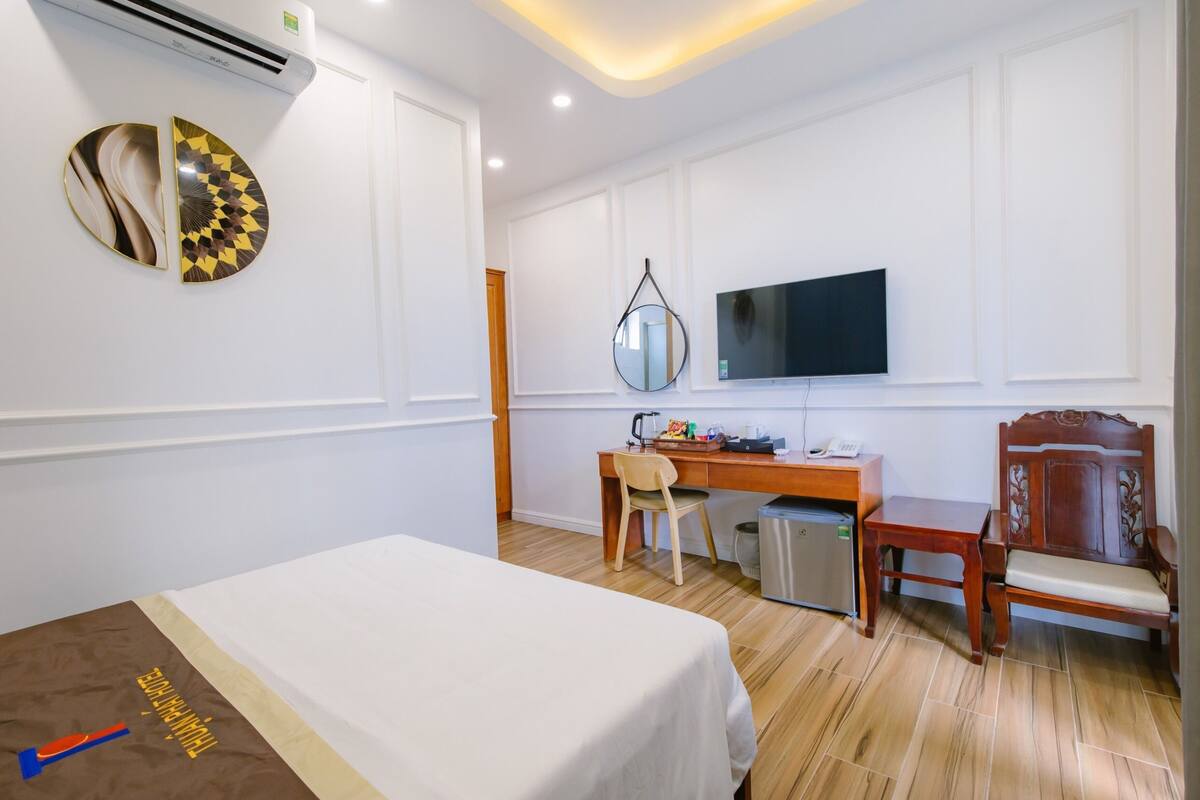 A hotel room with a bed, a desk with a chair, a television, and a mirror on the wall.
