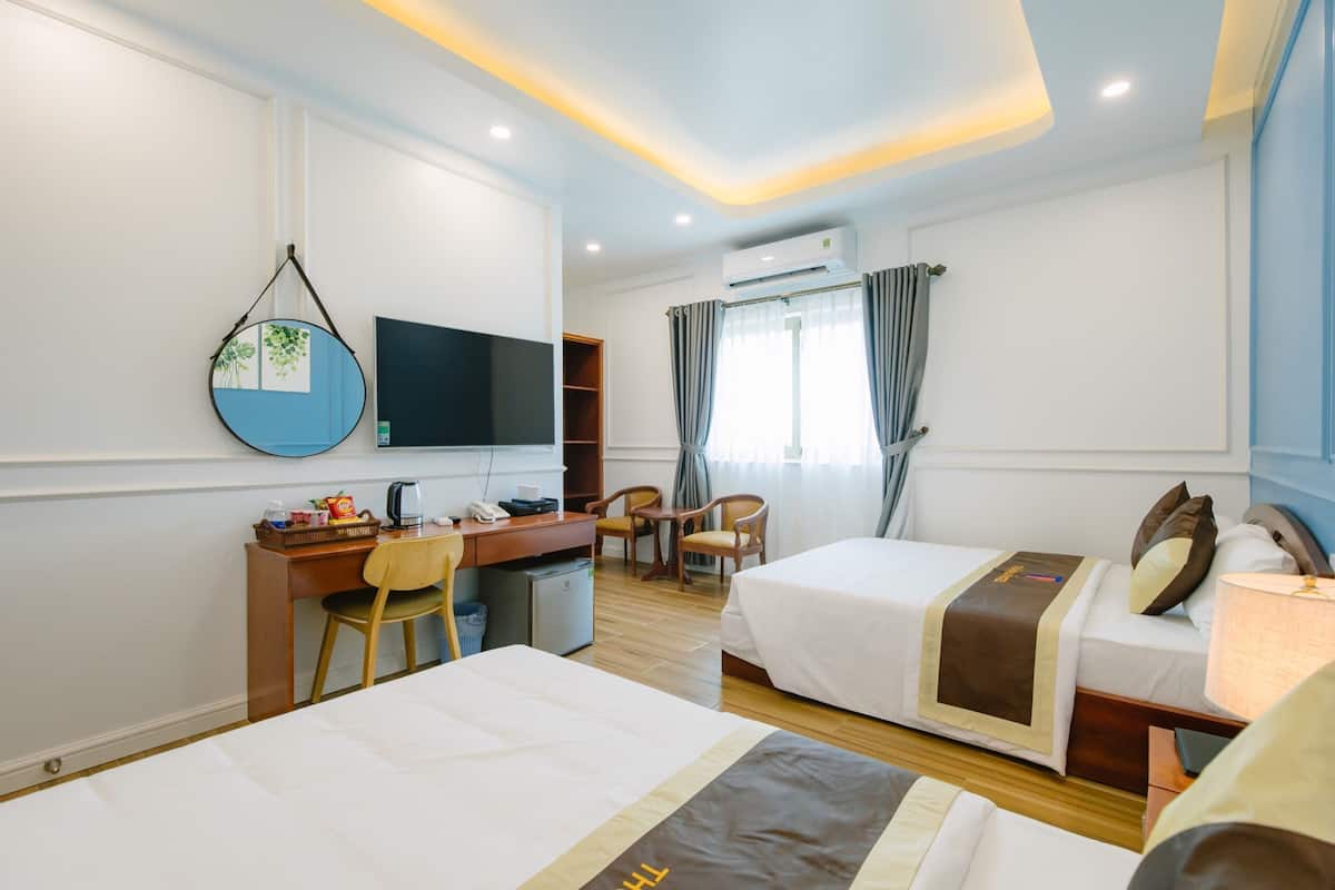 A hotel room with two beds, a desk with a chair, a television, and an air conditioning unit.