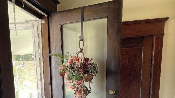 Eine Holztür mit einer Milchglasplatte und einem hängenden Blumenarrangement.