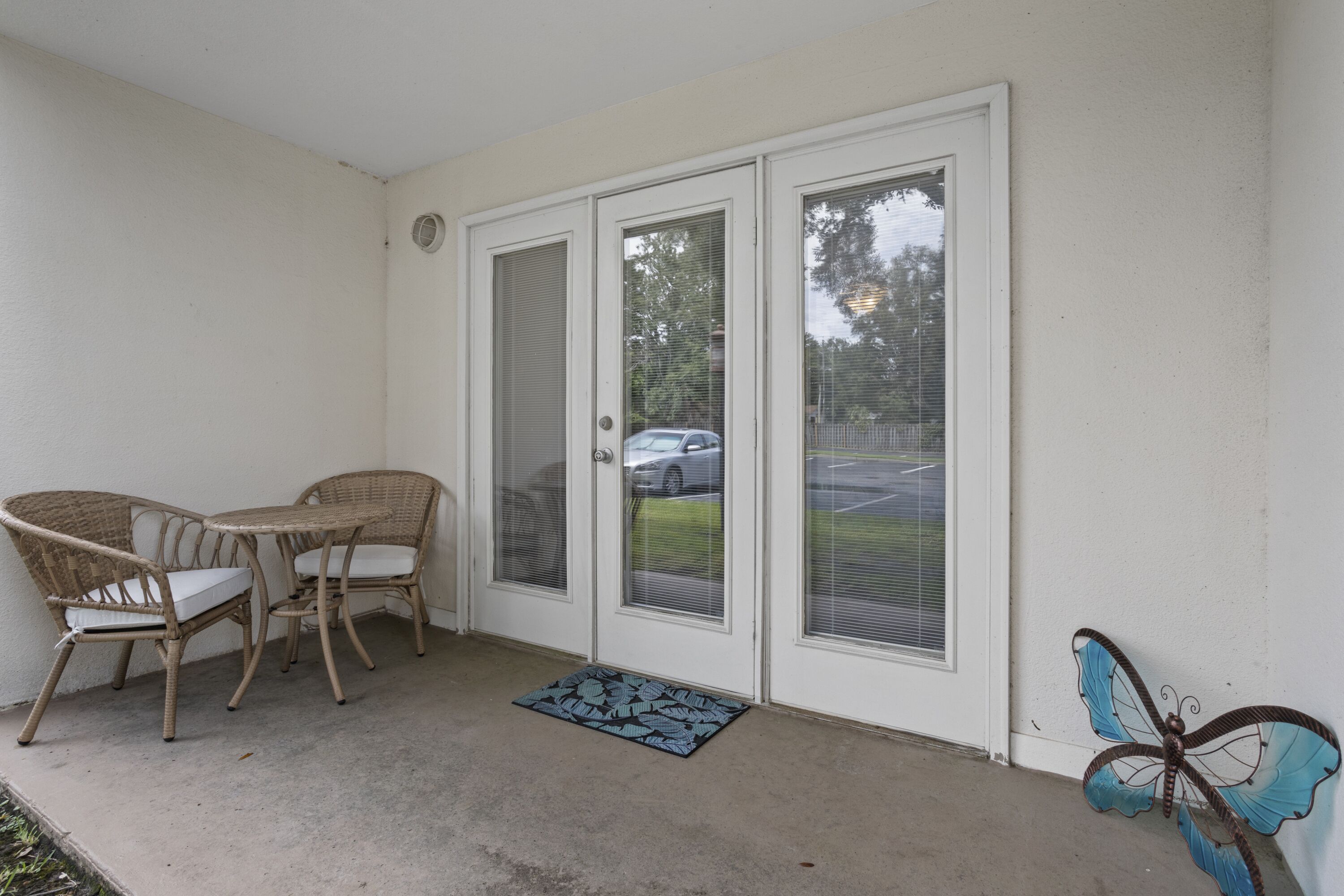 A covered patio with two wicker chairs and a small table, a butterfly decoration, and a door with a window.