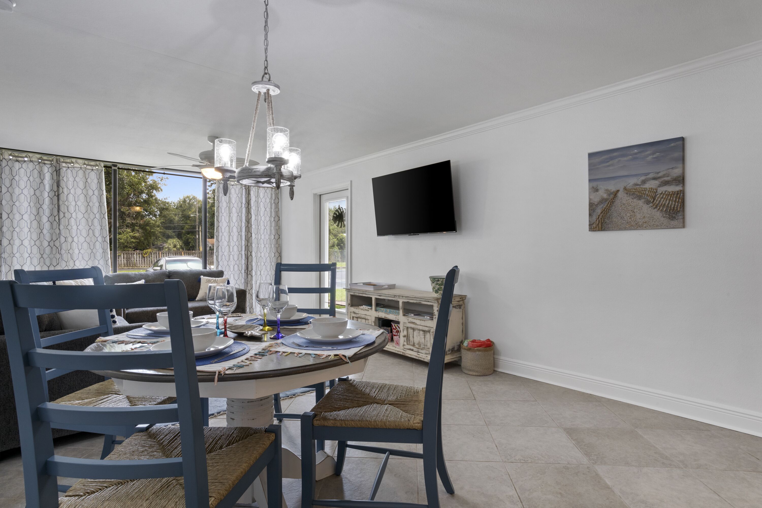 A dining area with a round table, chairs, a chandelier, a flat-screen TV, and a painting on the wall.