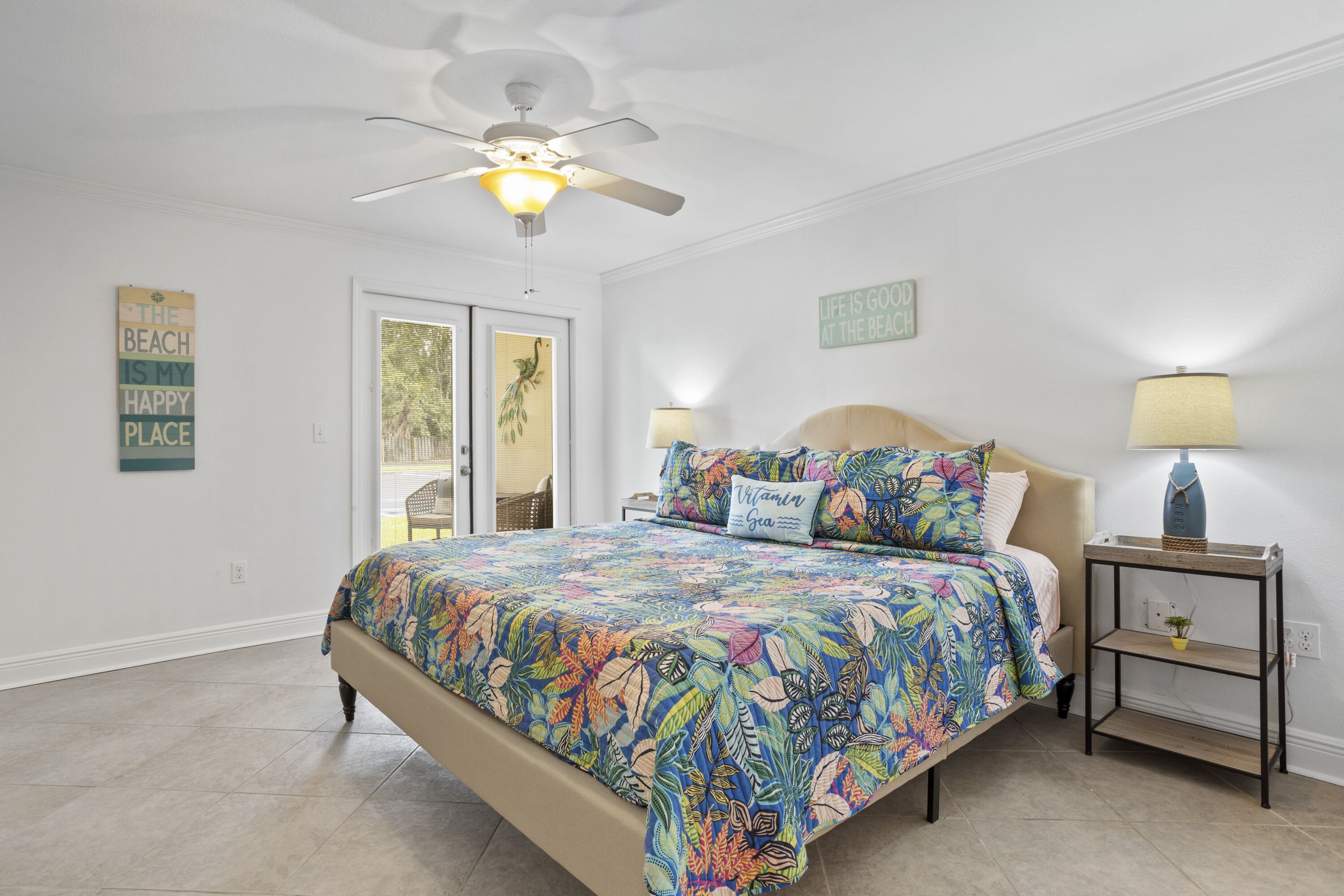 A bedroom with a bed, a ceiling fan, a nightstand with a lamp, and two wall decorations.