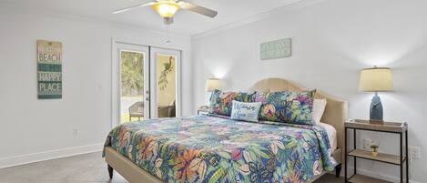 A bedroom with a bed, a ceiling fan, a nightstand with a lamp, and two wall decorations.