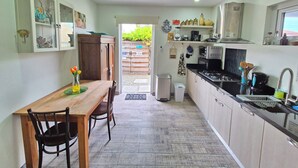 A compact kitchen with a wooden table and chairs, a built-in oven, and a sink. - Cozy modern apartment w/BBQ grill - 4min from the beach! (Noord)