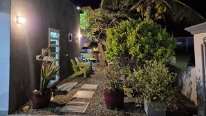 A nighttime outdoor area with a palm tree, potted plants, and a seating area with chairs and a table. - Cozy modern apartment w/BBQ grill - 4min from the beach! (Noord)