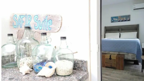 A room with a bed, a nightstand, and a sign reading "SAFIR Suite". - Cozy modern apartment w/BBQ grill - 4min from the beach! (Noord)