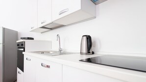 A modern kitchen with white cabinets, a stainless steel refrigerator, a built-in oven, a sink with a faucet, and a kettle.