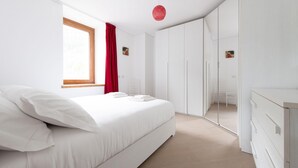 A modern bedroom with a large bed, a wardrobe, and a mirror.
