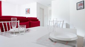 A dining table set with white plates, clear glasses, and a fork, with a red upholstered sofa in the background.