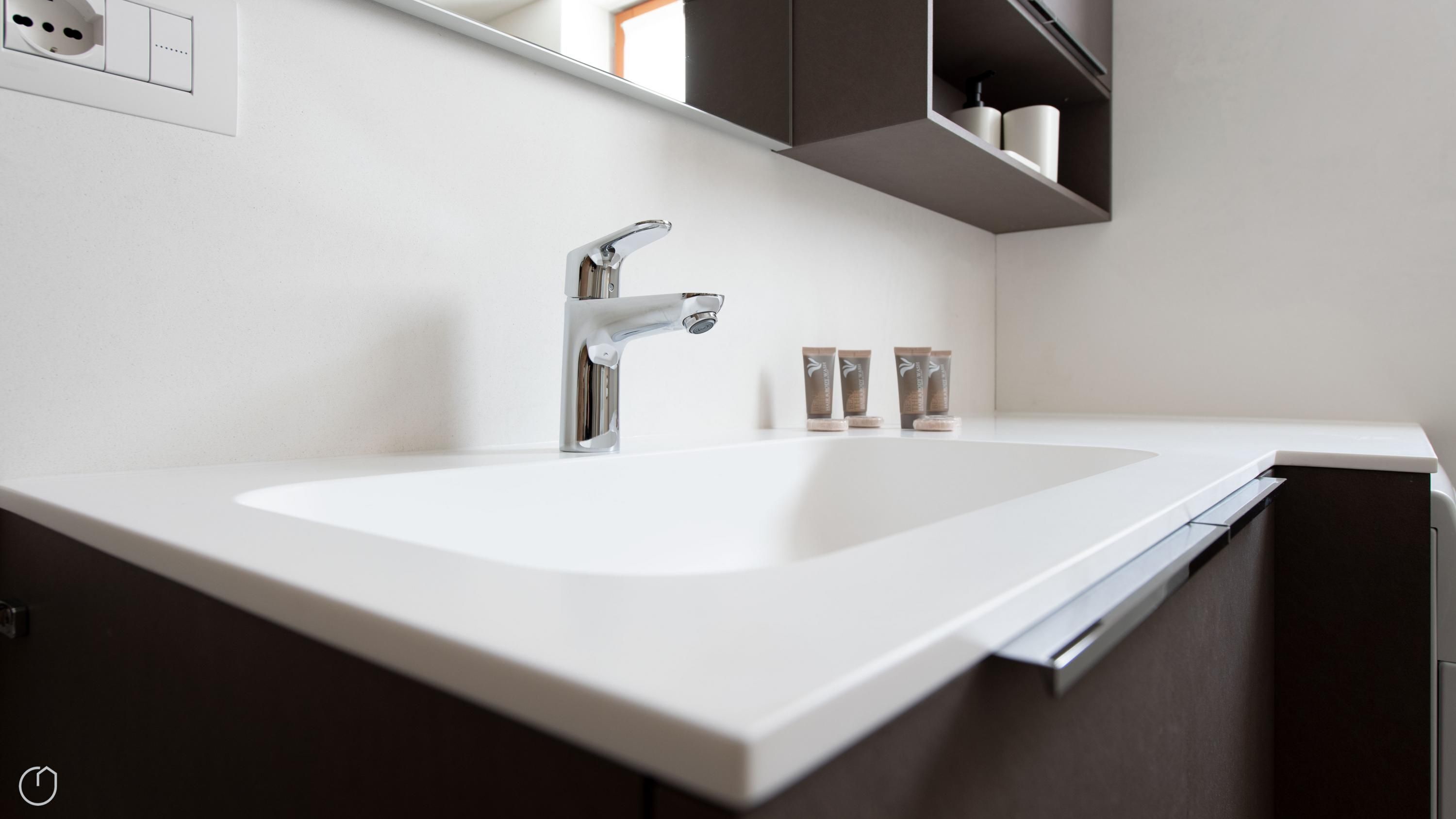 A modern bathroom with a white sink, chrome faucet, and dark cabinetry.