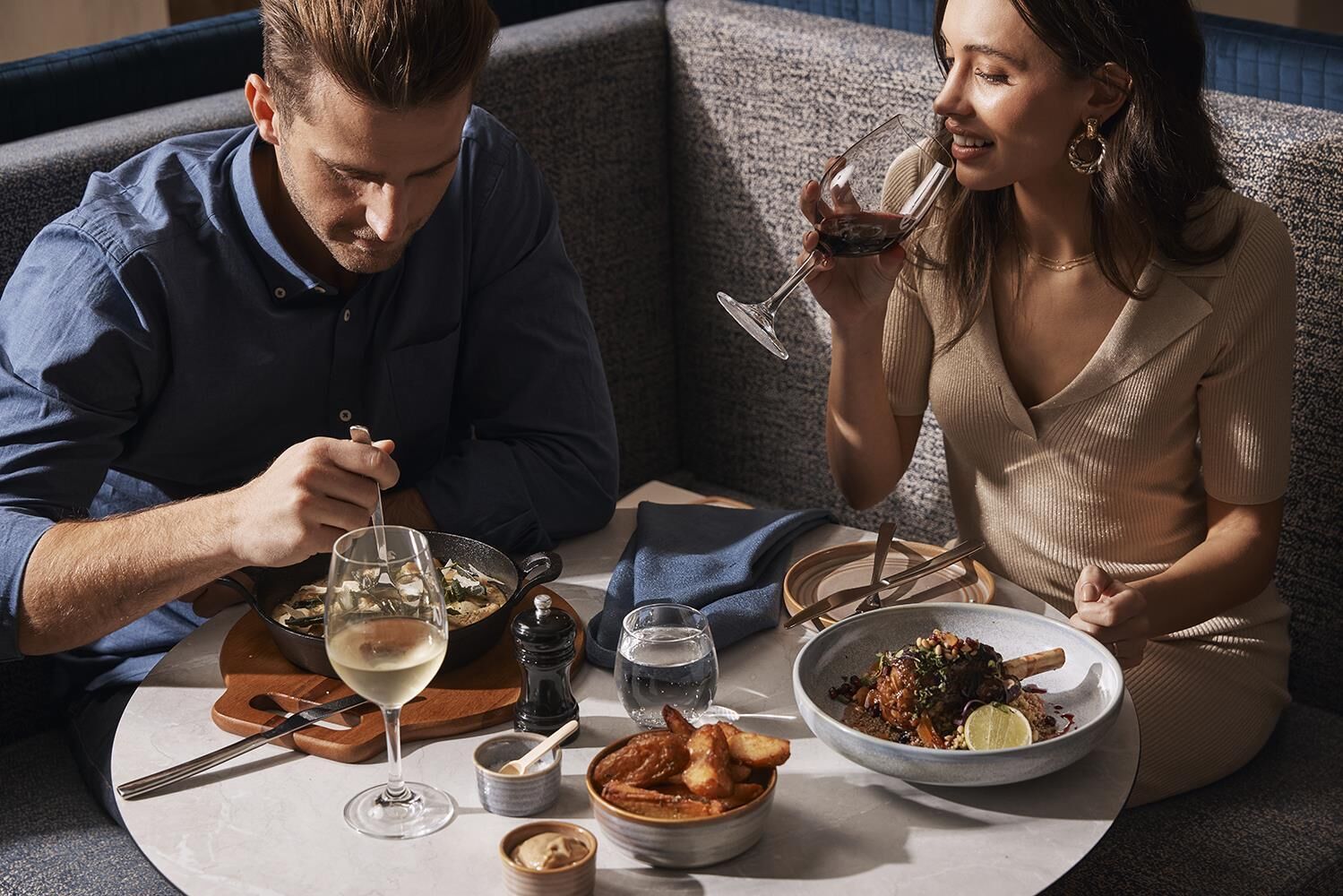 A couple dining at a table with a variety of dishes and drinks.