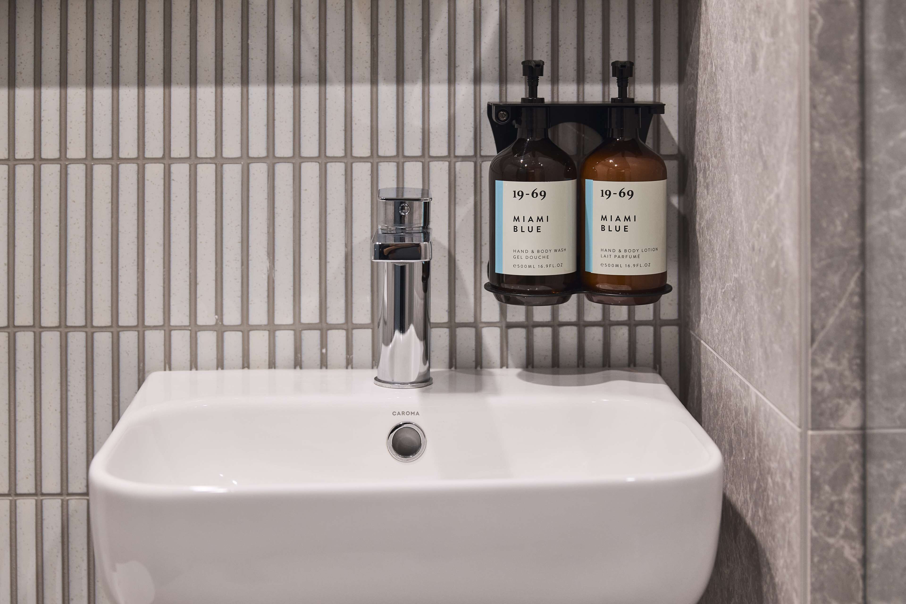 A bathroom sink with a faucet and two bottles of Miami Blue hand and body wash.