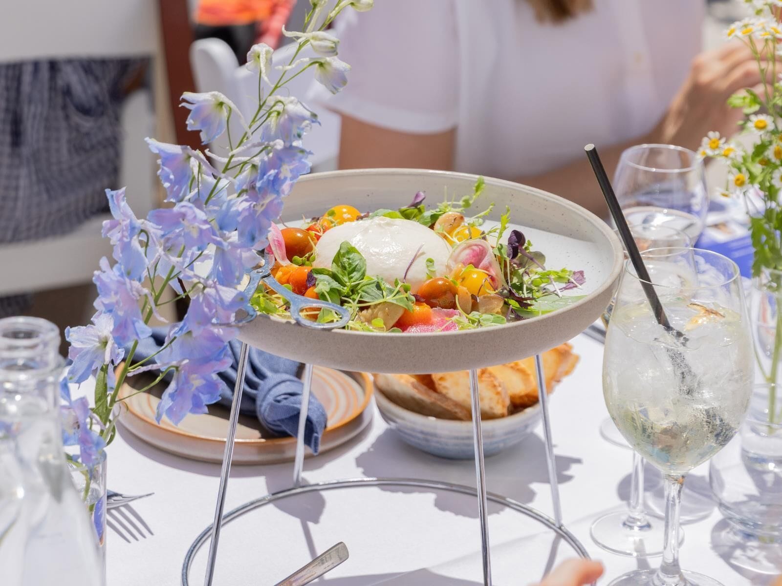 Une table à manger avec une assiette de nourriture, un verre et un vase de fleurs.