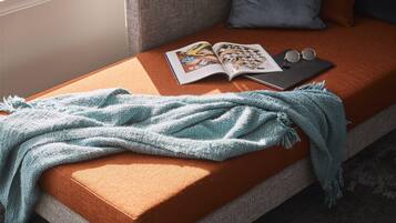 A cozy reading nook with a cushioned bench, a blanket, a magazine, and a pair of glasses.