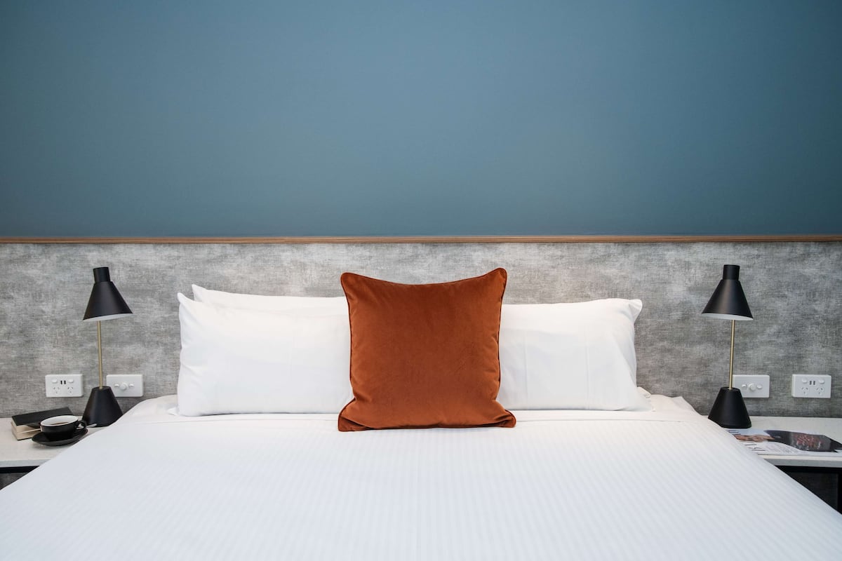 A neatly made bed with white and brown pillows, two black bedside lamps, and a grey textured wall.