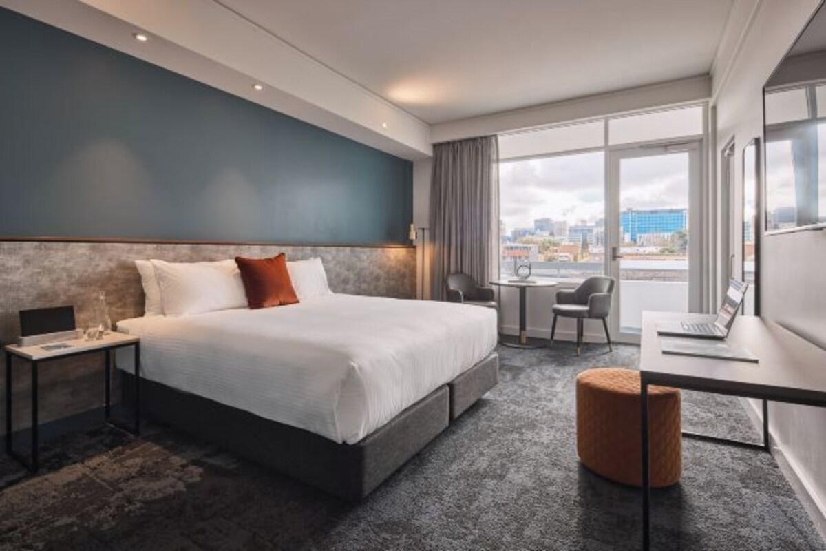 Quarto de hotel moderno com uma cama grande, uma escrivaninha e vista para a cidade.
