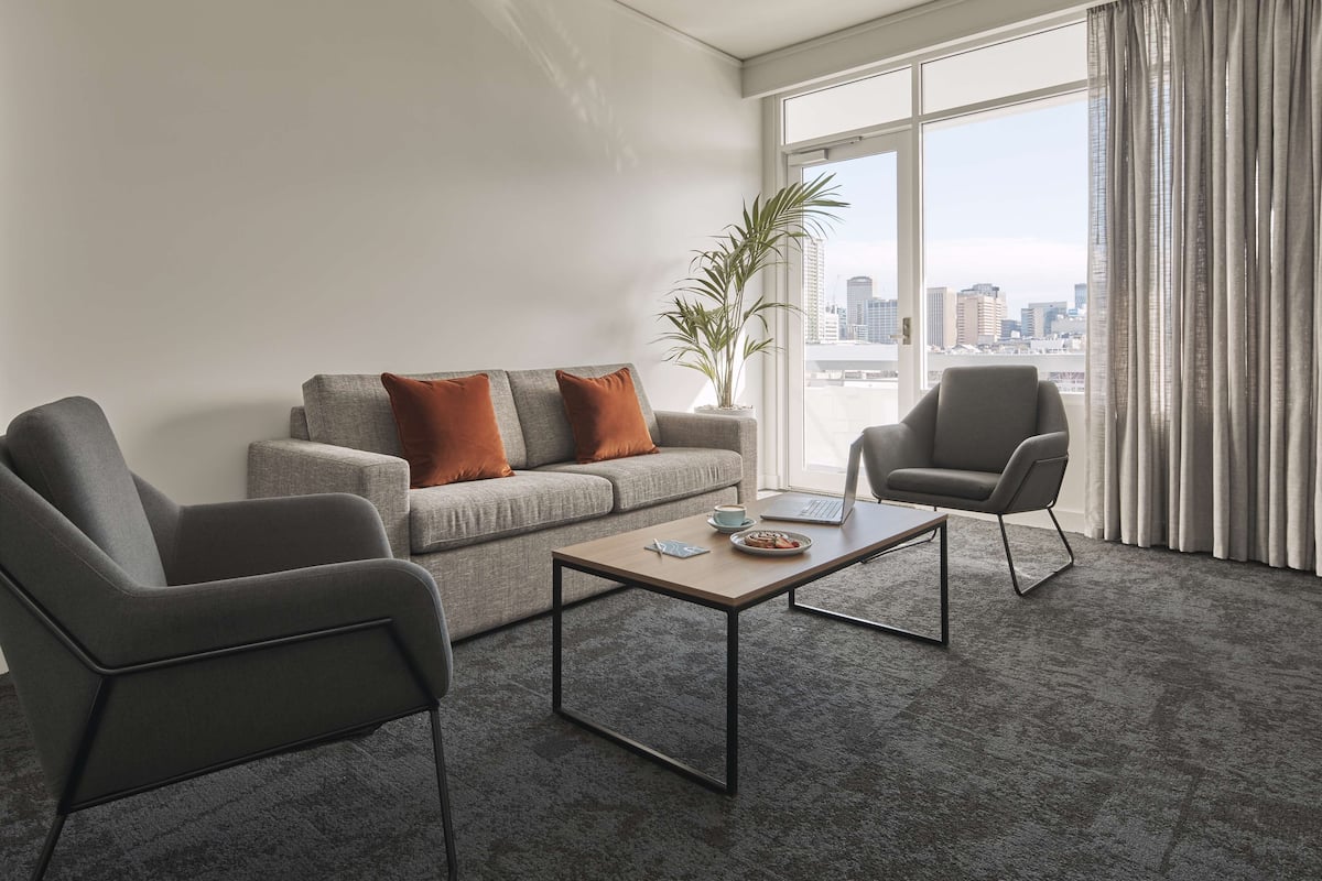 A modern living room with a grey sofa, two armchairs, a coffee table, and a city view through large windows.