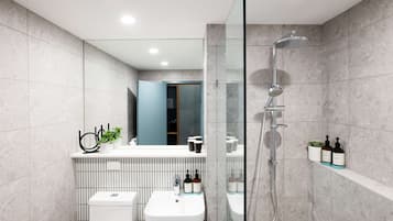 Un baño moderno con lavamanos blanco, ducha con cerramiento de vidrio y espejo sobre el lavamanos.