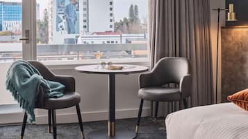 A hotel room with a large window, two chairs, a round table, and a bed.