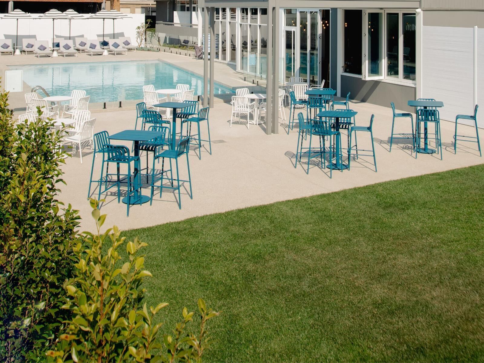 A poolside area with multiple seating arrangements, including tables and chairs, and a glass-enclosed building in the background.
