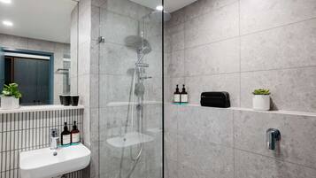 A modern bathroom with a glass-enclosed shower, a white sink, and toiletries on a shelf.