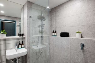 Une salle de bain moderne avec une douche à parois de verre, un lavabo blanc et des articles de toilette rangés sur une étagère.