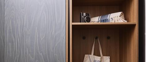 A wooden wardrobe with a grey patterned door, a camera, a folded towel, and a beige tote bag with blue accents.