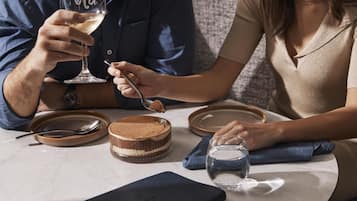 Una mesa de comedor con un postre, una copa de vino blanco y un teléfono inteligente.