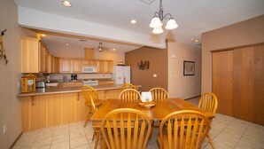 A dining area with a wooden table and chairs, a kitchen in the background, and a ceiling fan. - Foothills Home (Yuma)