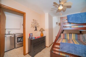 A compact room with a bunk bed, a washing machine, a dresser, and a ceiling fan.