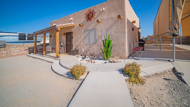 A building with a patio area, a large plant, and a decorative wall feature. - Foothills Home (Yuma)
