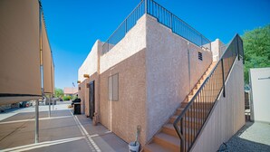 A building with a staircase leading to a second floor, a covered outdoor area, and a small garden area. - Foothills Home (Yuma)