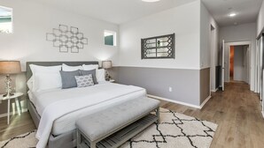 Un dormitorio moderno con una cama grande, mesitas de noche, un espejo en la pared y un pasillo que lleva a otra habitación.